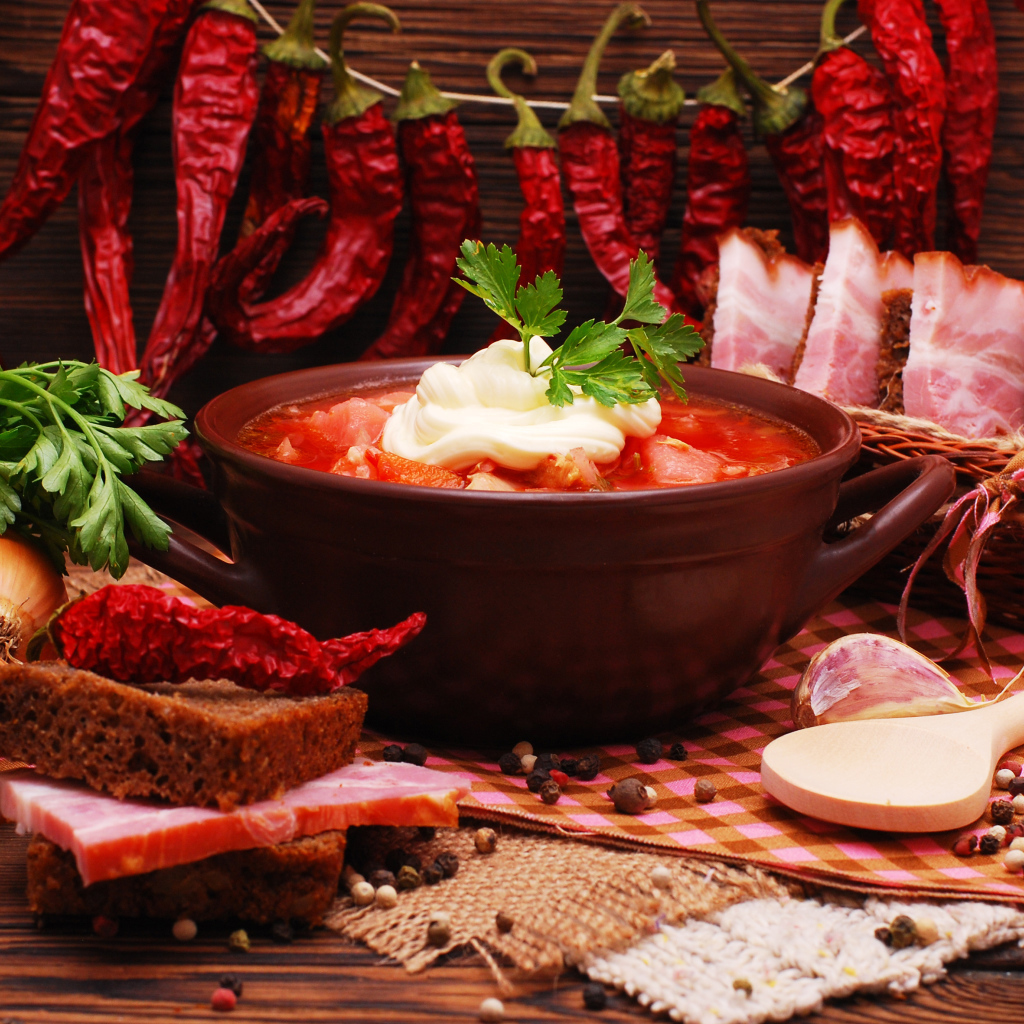 Тарелка борща на столе с красным острым перцем, чесноком, луком, зеленью и бужениной