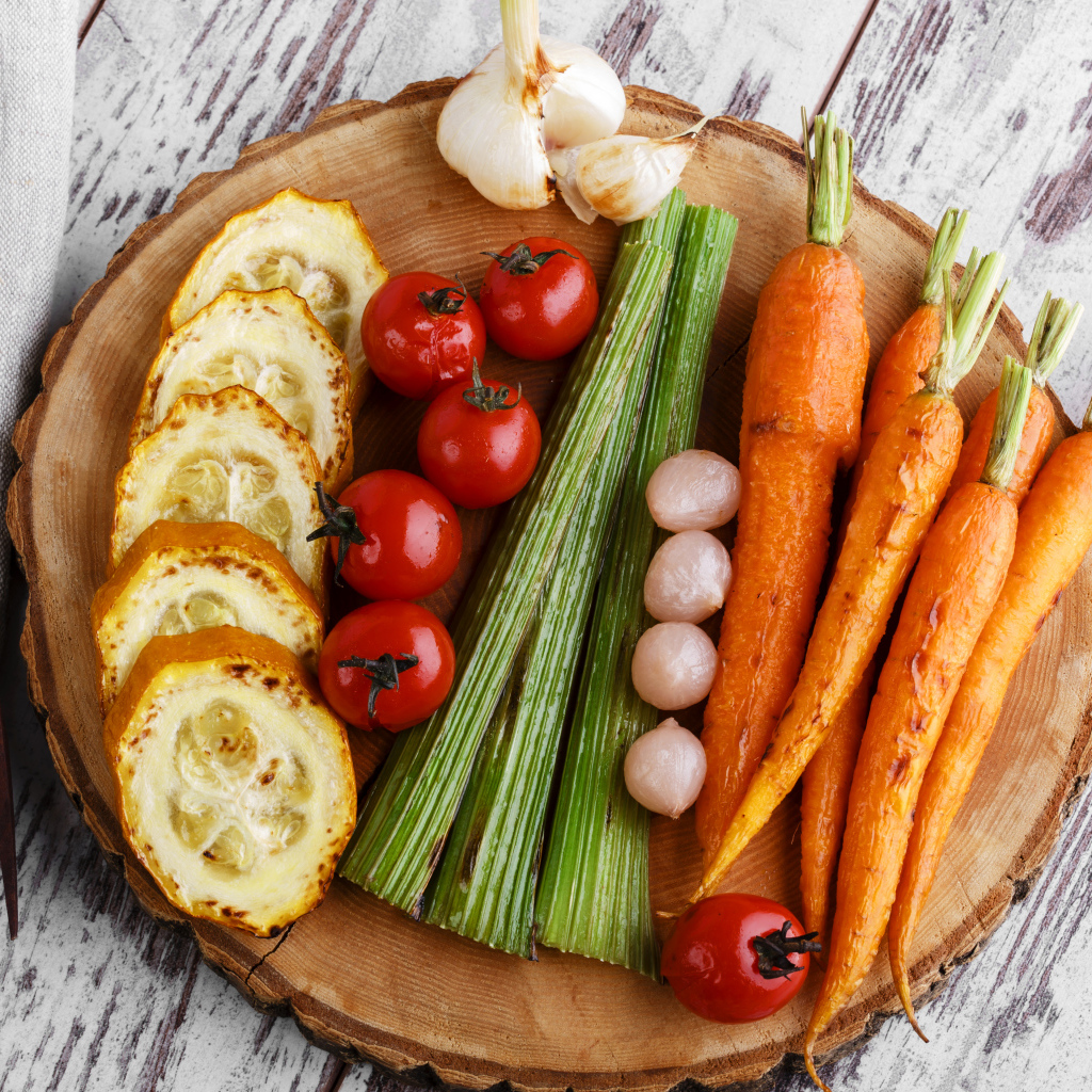 Печеные кабачки, помидоры, морковь, сельдерей и чеснок на разделочной доске
