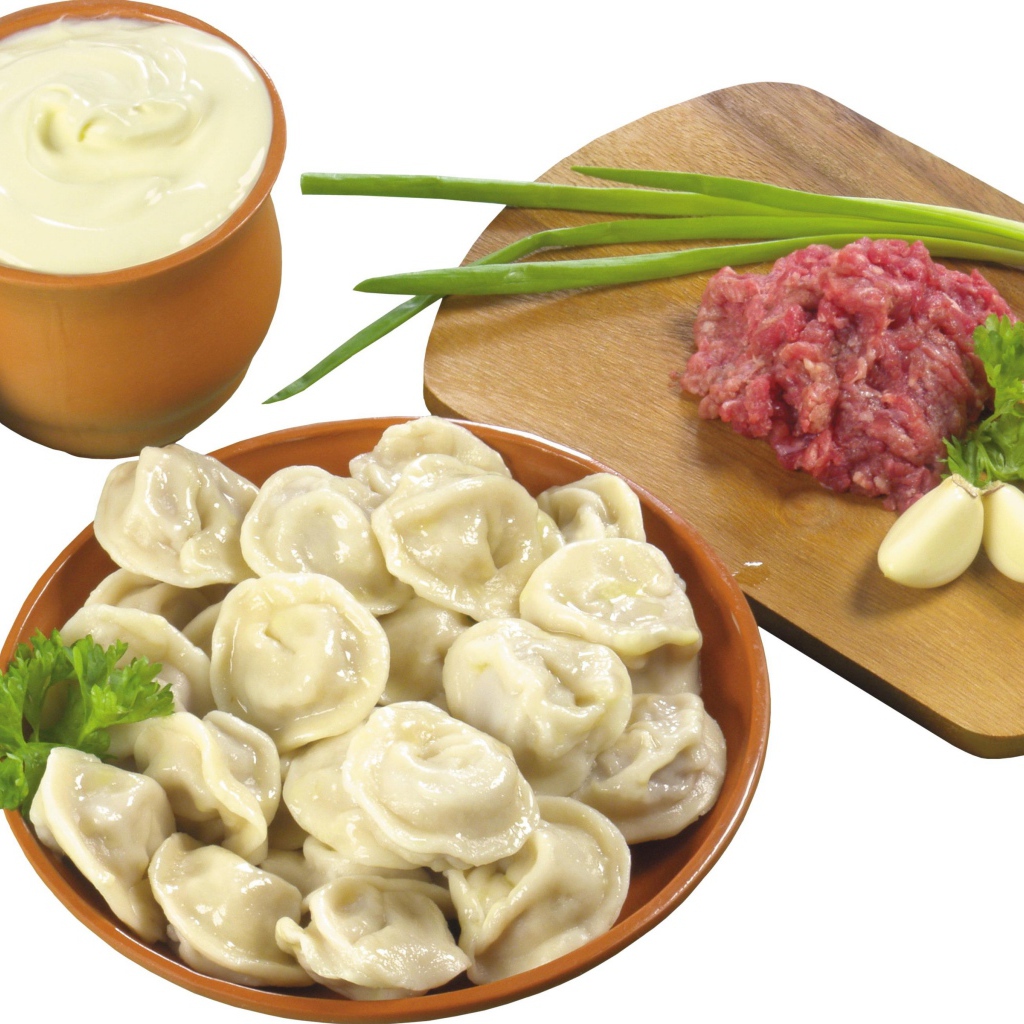 Вареные пельмени на столе с фаршем, сметаной и зеленым луком
