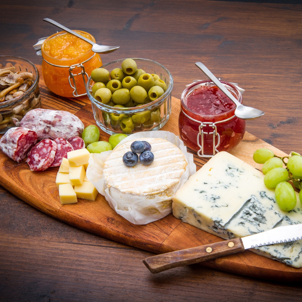 Сыр, грибы, маслины, колбаса, виноград и джем на разделочной доске 