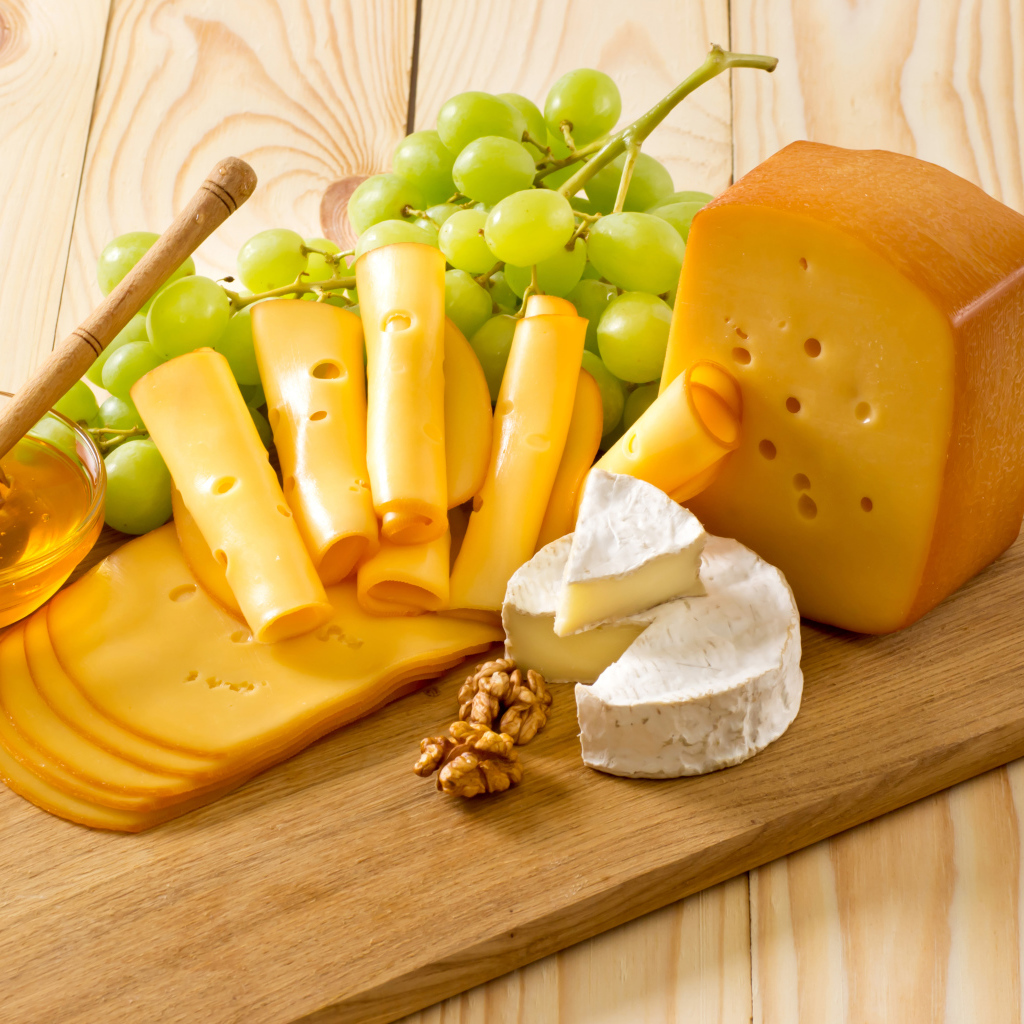 Сыр на столе с белым виноградом, медом и орехами 