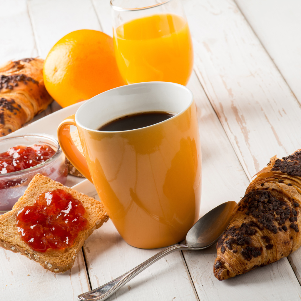 Coffee on a wooden table with croissants, juice and jam