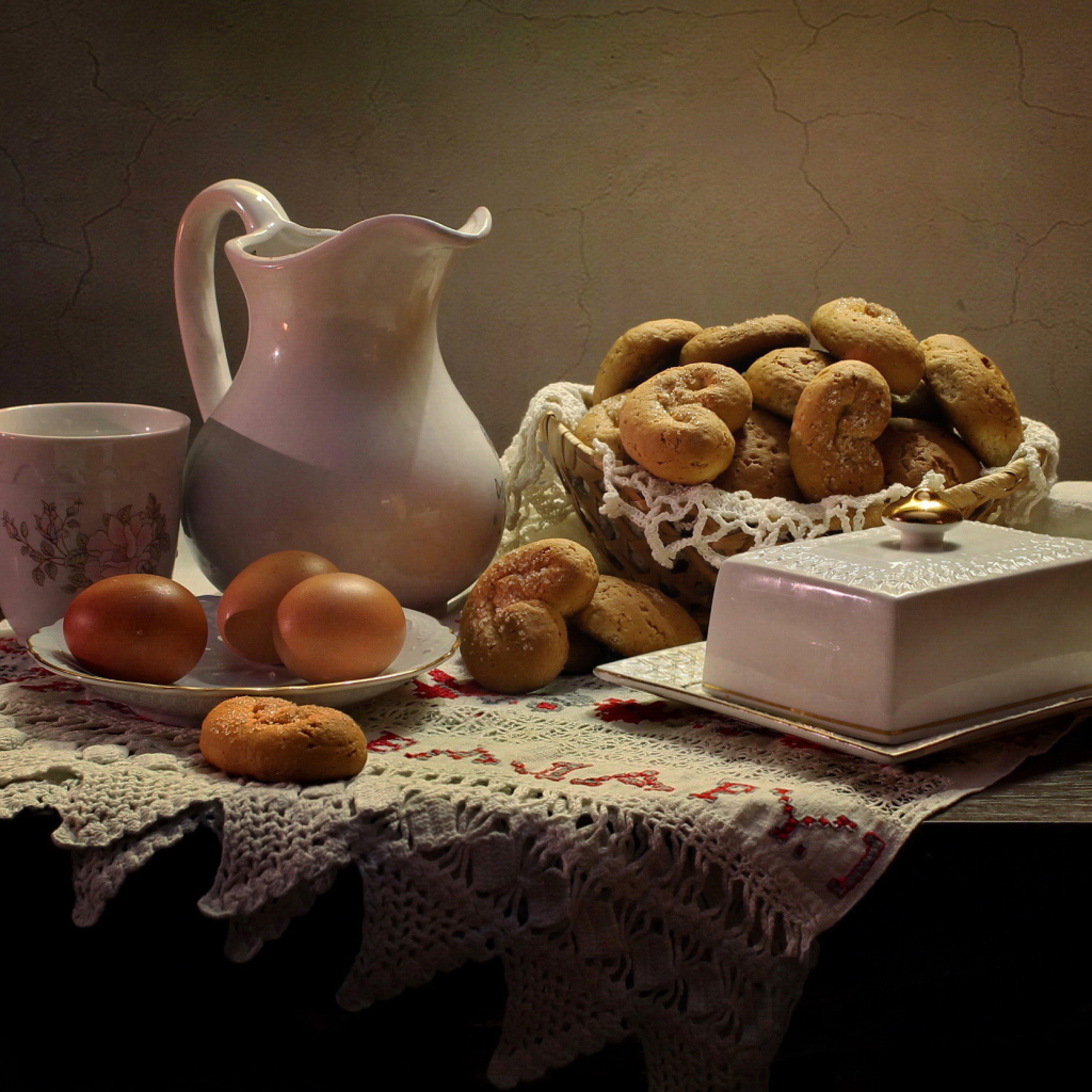 Вареные яйца на столе с кувшином, выпечкой и масленкой 