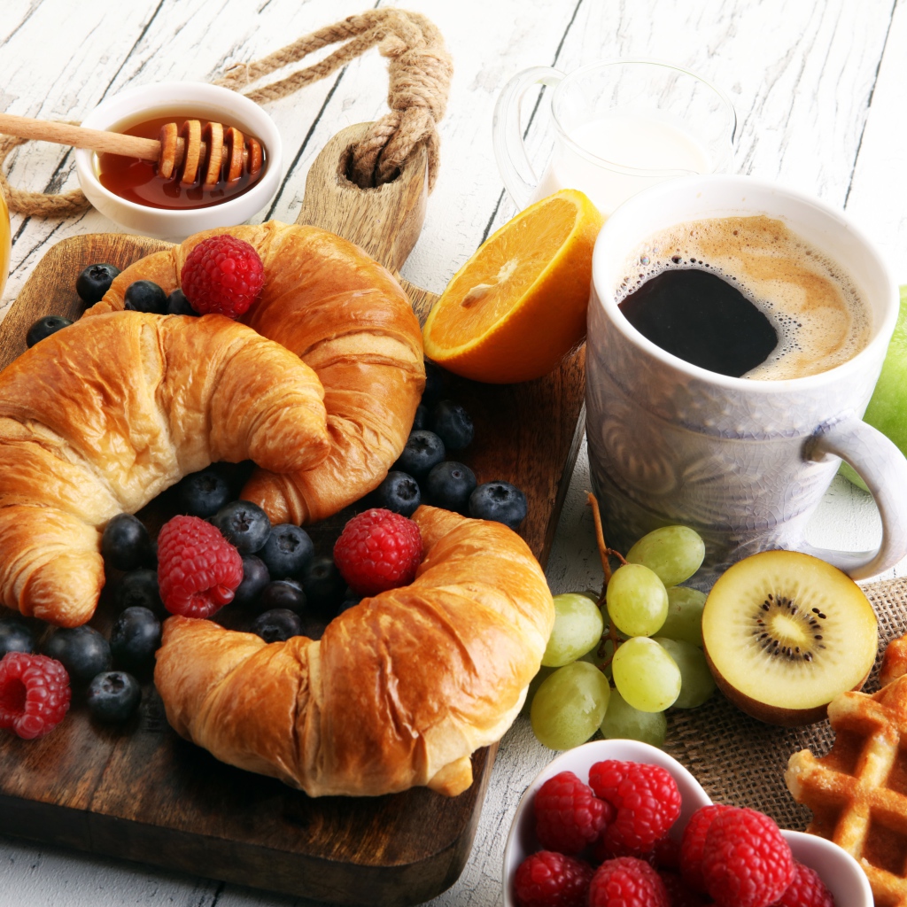 Croissants with berries, on the table with coffee, honey and waffles