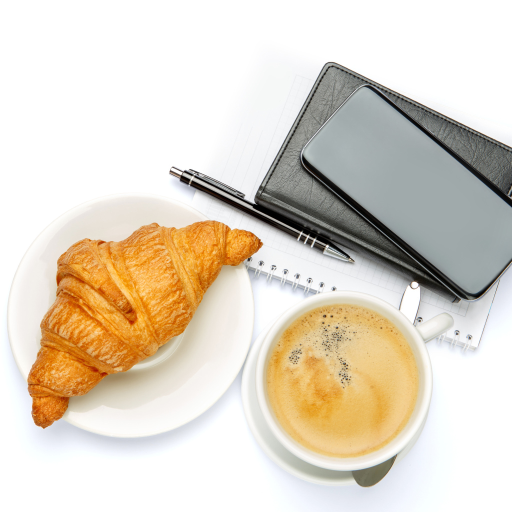 Чашка кофе, круассан, блонтон и смартфон на белом 