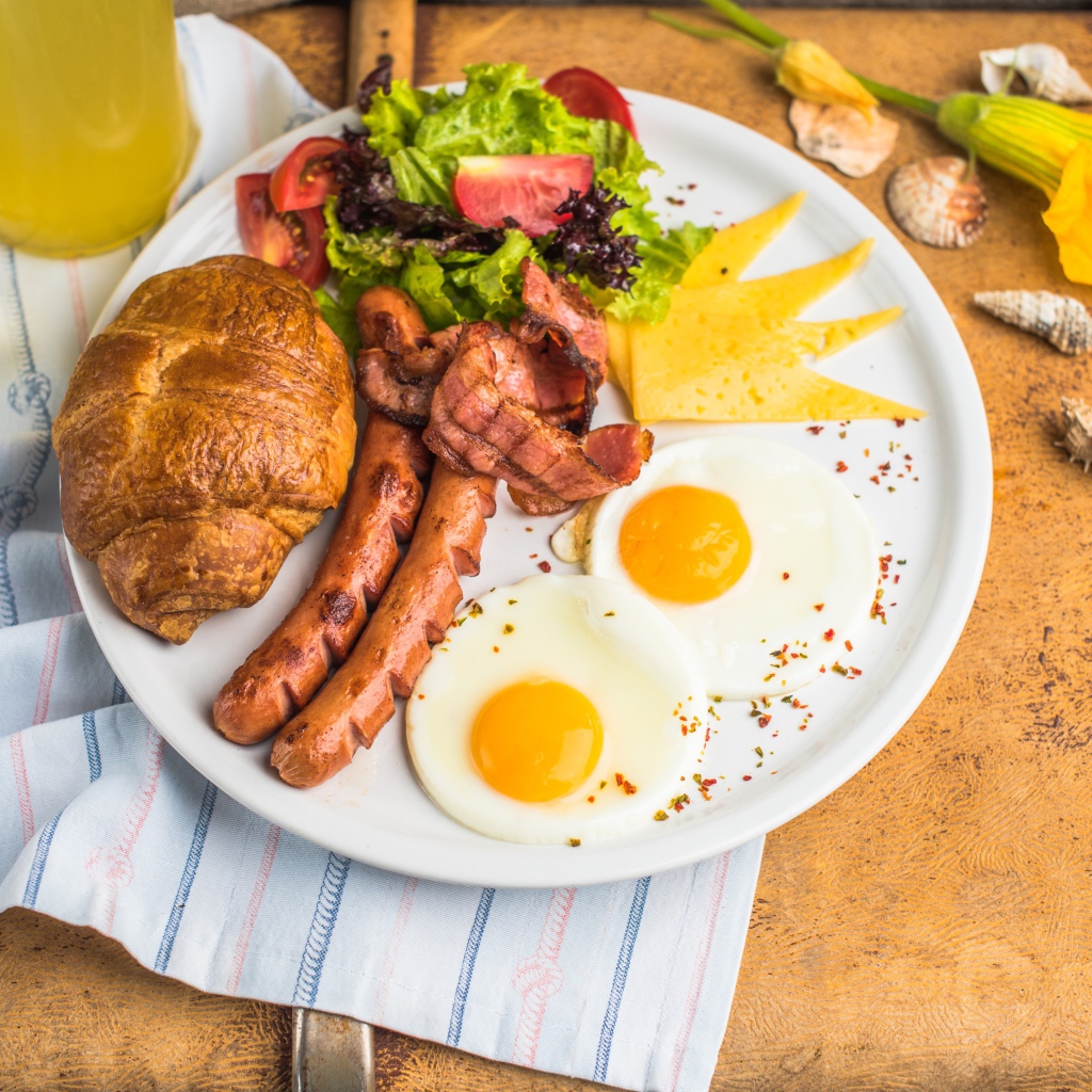Яичница, салат, сосиски и круассан с соком на завтрак 