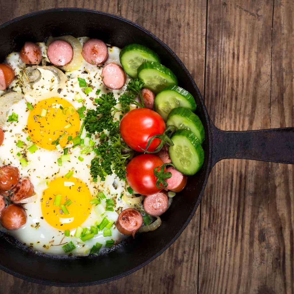 Яичница в сковороде с овощами и кусочками сосиски