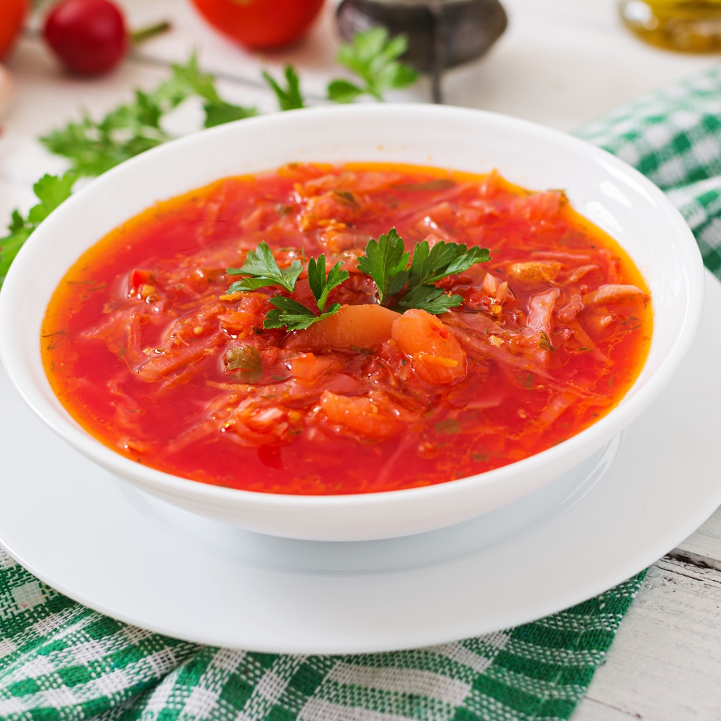 Горячий борщ с зеленью в белой тарелке на столе