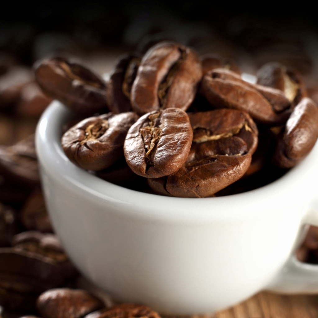 Много кофейных зерен в белой чашке на столе