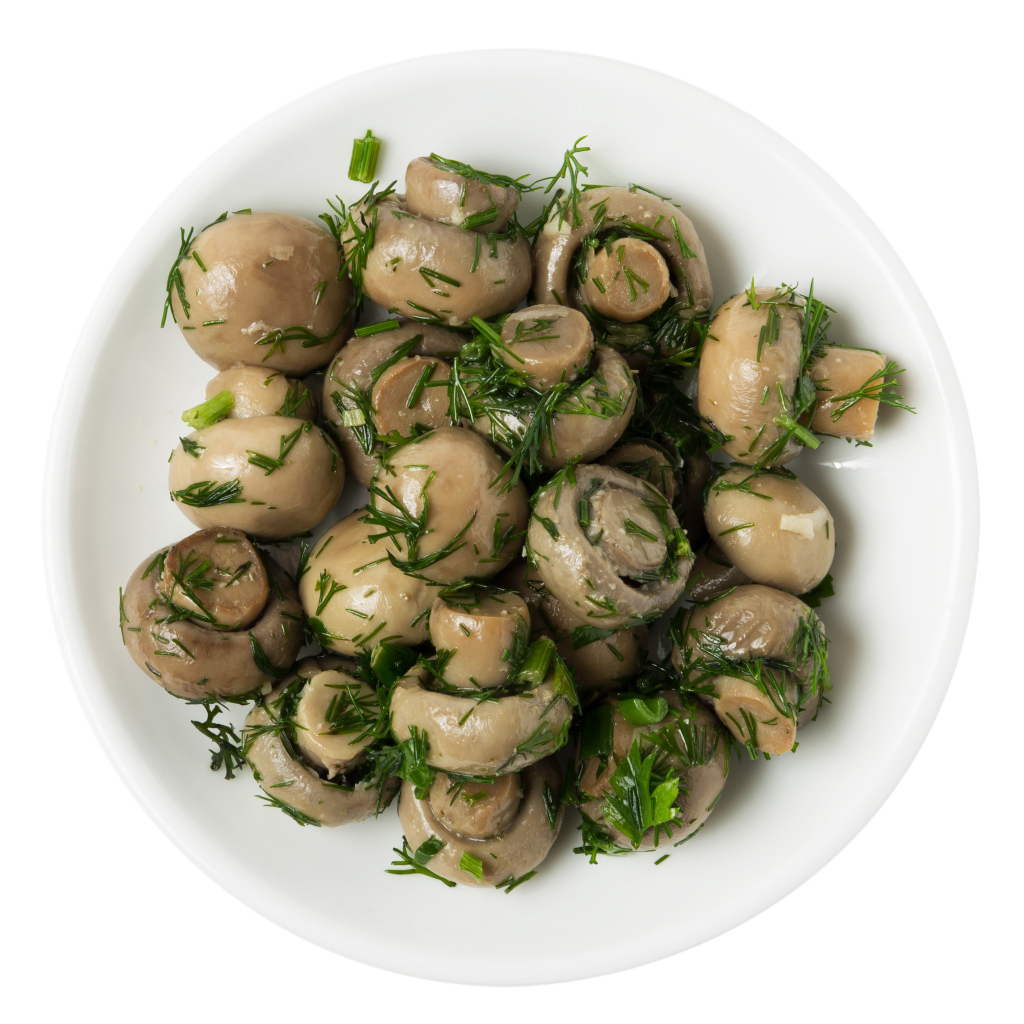 Маринованные шампиньоны с зеленью в белой тарелке на белом фоне 