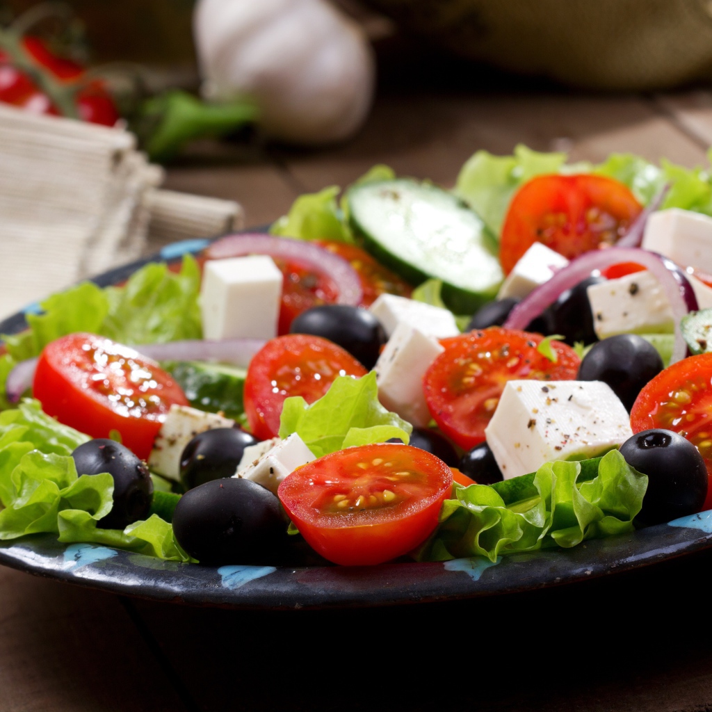 Салат с помидорами, огурцами, оливками, кусочками сыра и луком на листьях салата