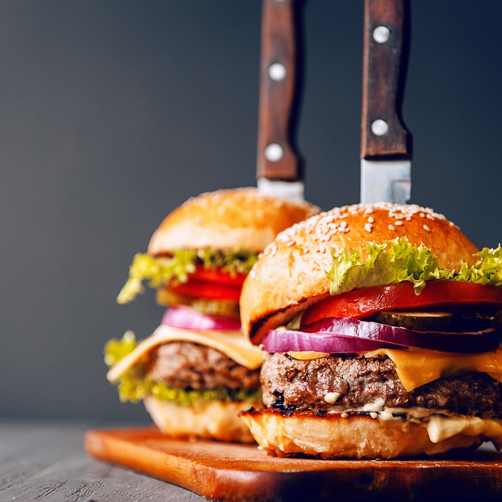 Два гамбургера с ножами на разделочной доске 