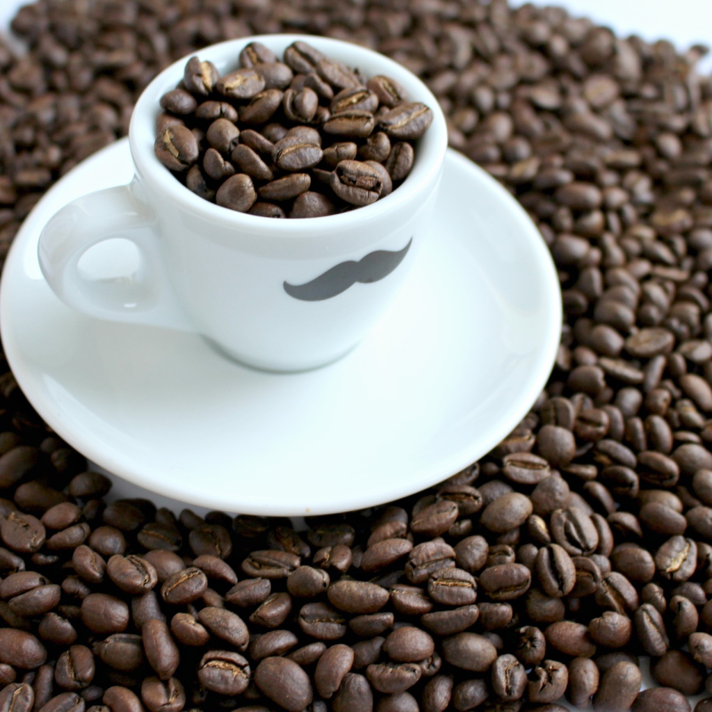 Белая чашка с жареными кофейными зернами стоит на столе с кофейными зернами