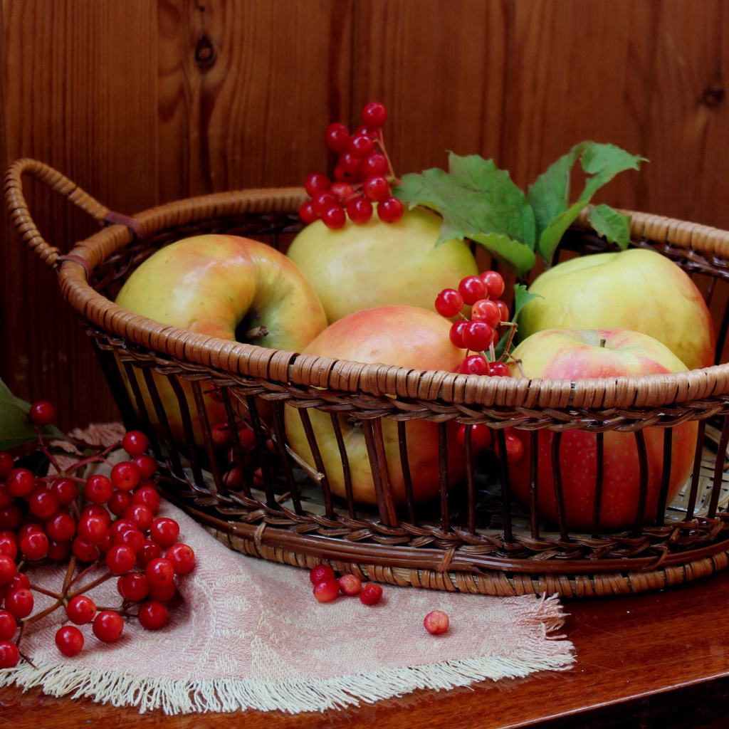 Красивые яблоки в корзине на столе с ягодами калины