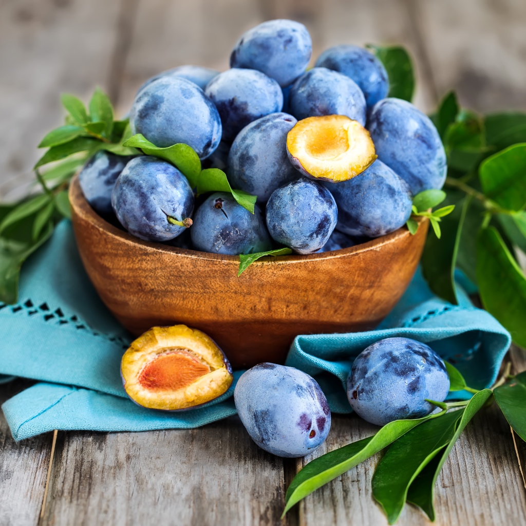 Синие сливы в деревянной миске с зеленой листвой