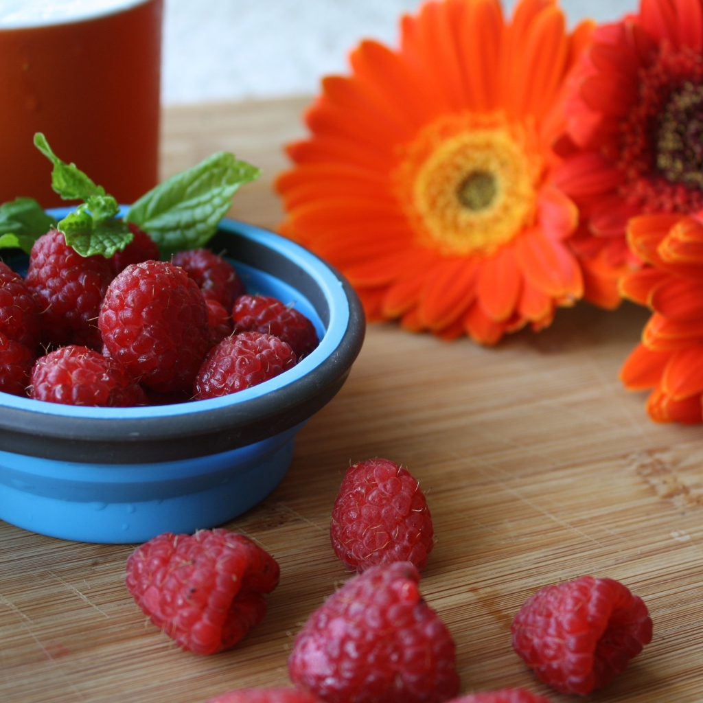 Свежая малина на столе с цветами герберы