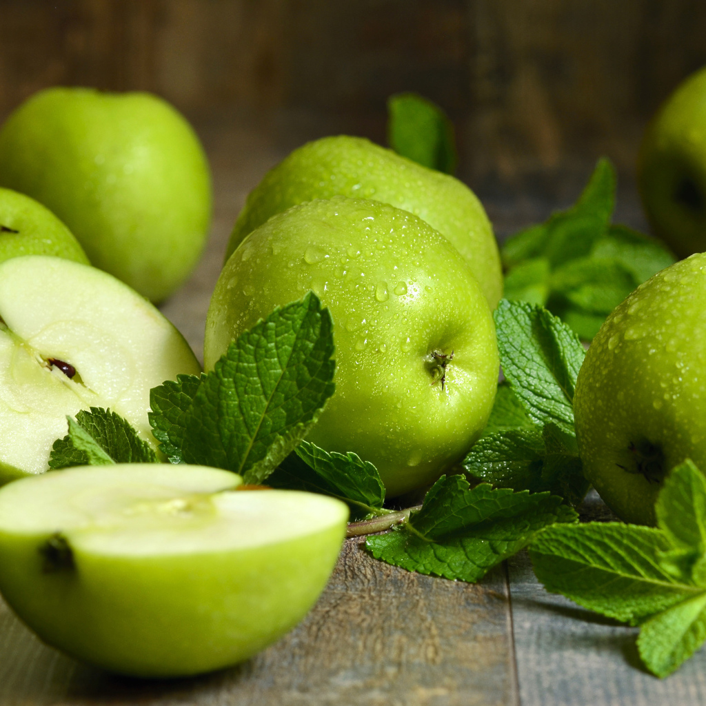 Зеленые яблоки в каплях воды на столе с мятой