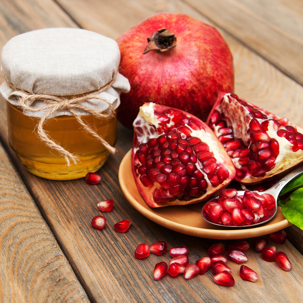 Гранат на деревянном столе с банкой меда