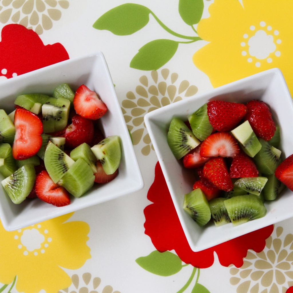 Салат с ягодами клубники и киви в белых тарелках на столе 