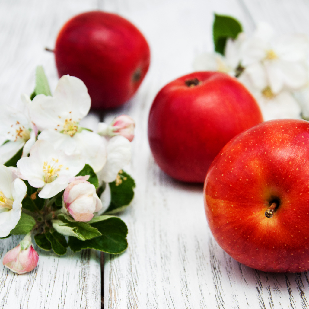 Три красных яблока с цветами на деревянной поверхности