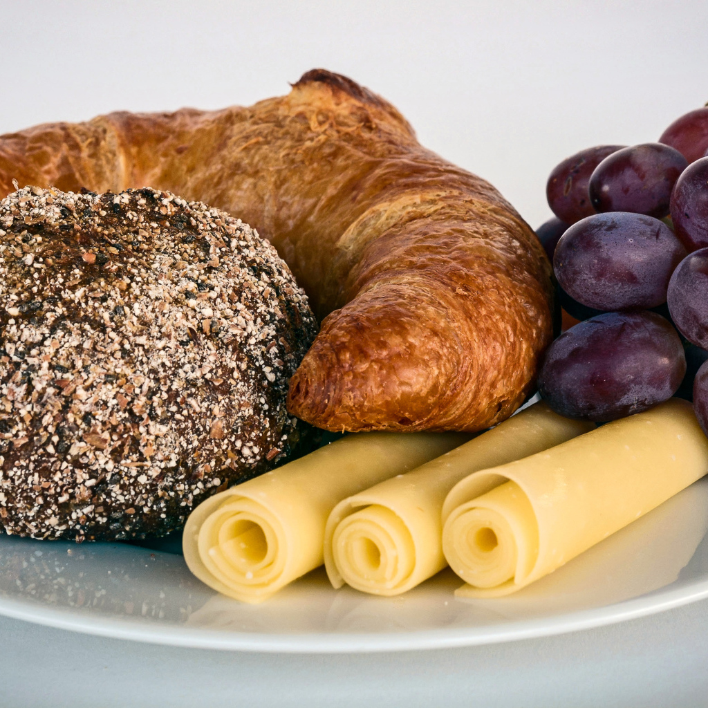 Свежая выпечка с сыром и розовым виноградом на белой тарелке 