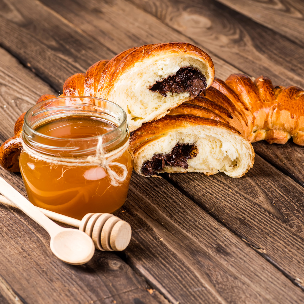 Банка меда, свежая выпечка и ложки на деревянном столе