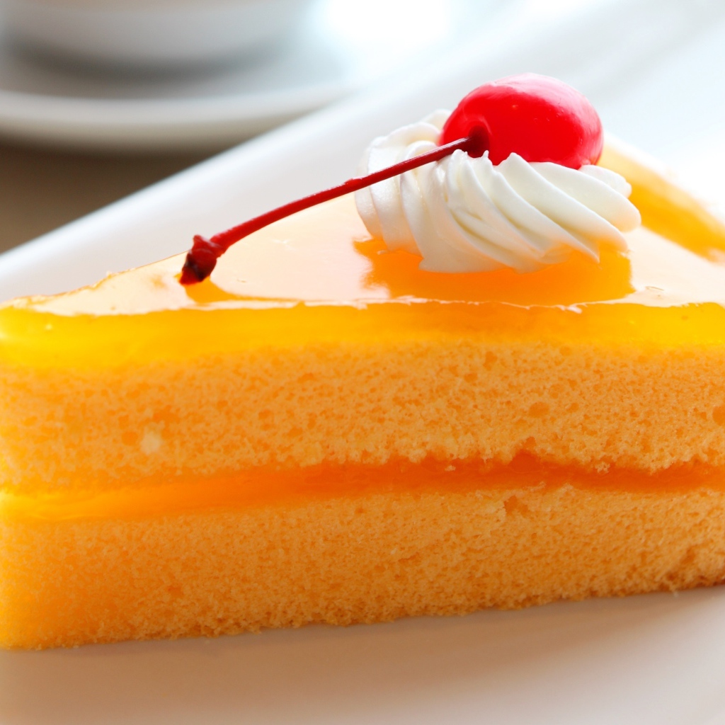 Кусок апельсинового торта с вишенкой на белой тарелке