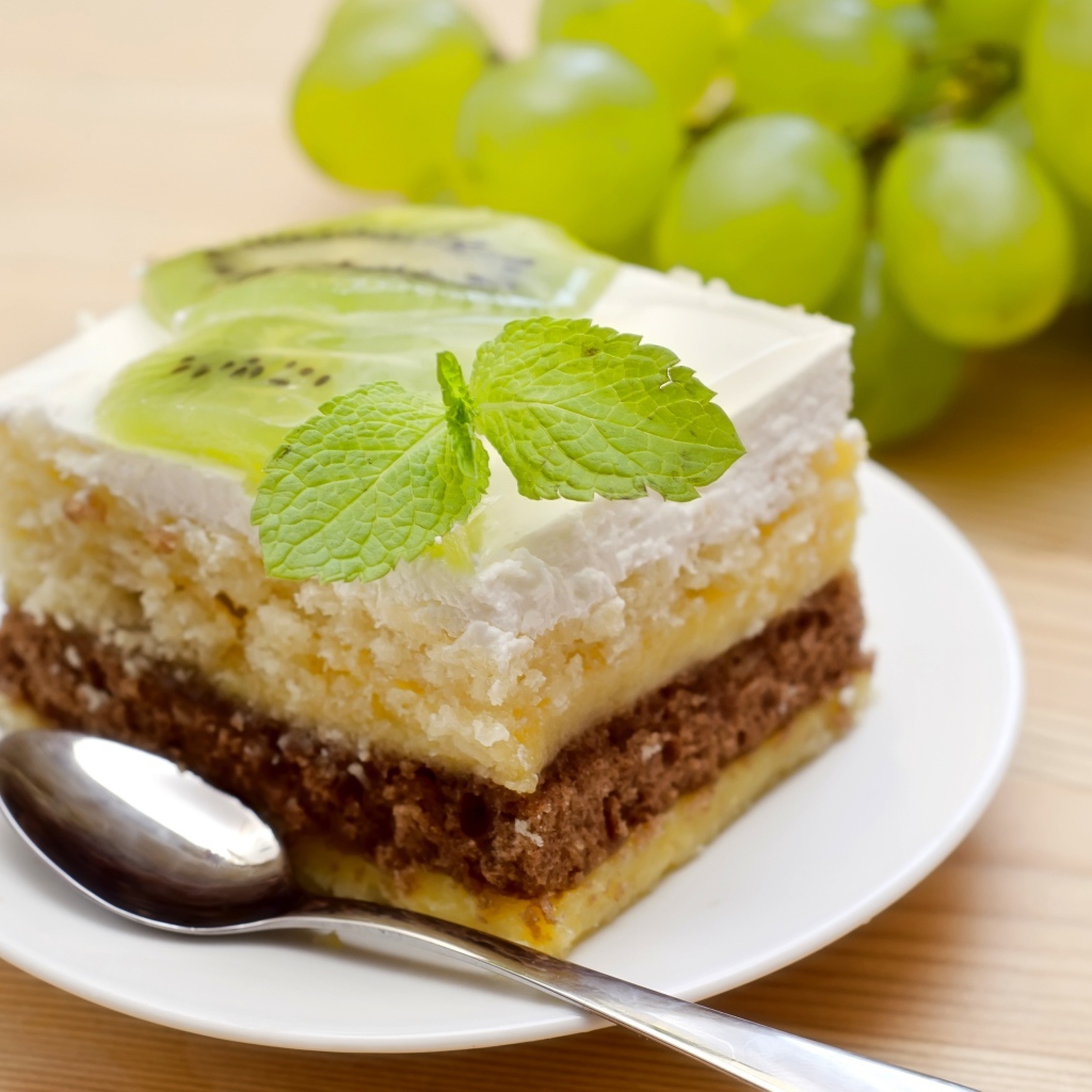 Кусок торта с киви и мятой на столе с виноградом