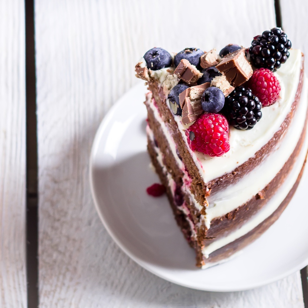 Кусок торта с ягодами малины и черники на блюдце