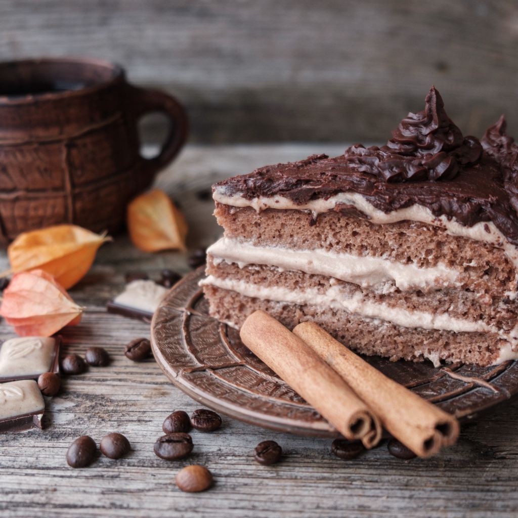 Кусок торта с корицей на столе с шоколадом и чашкой кофе
