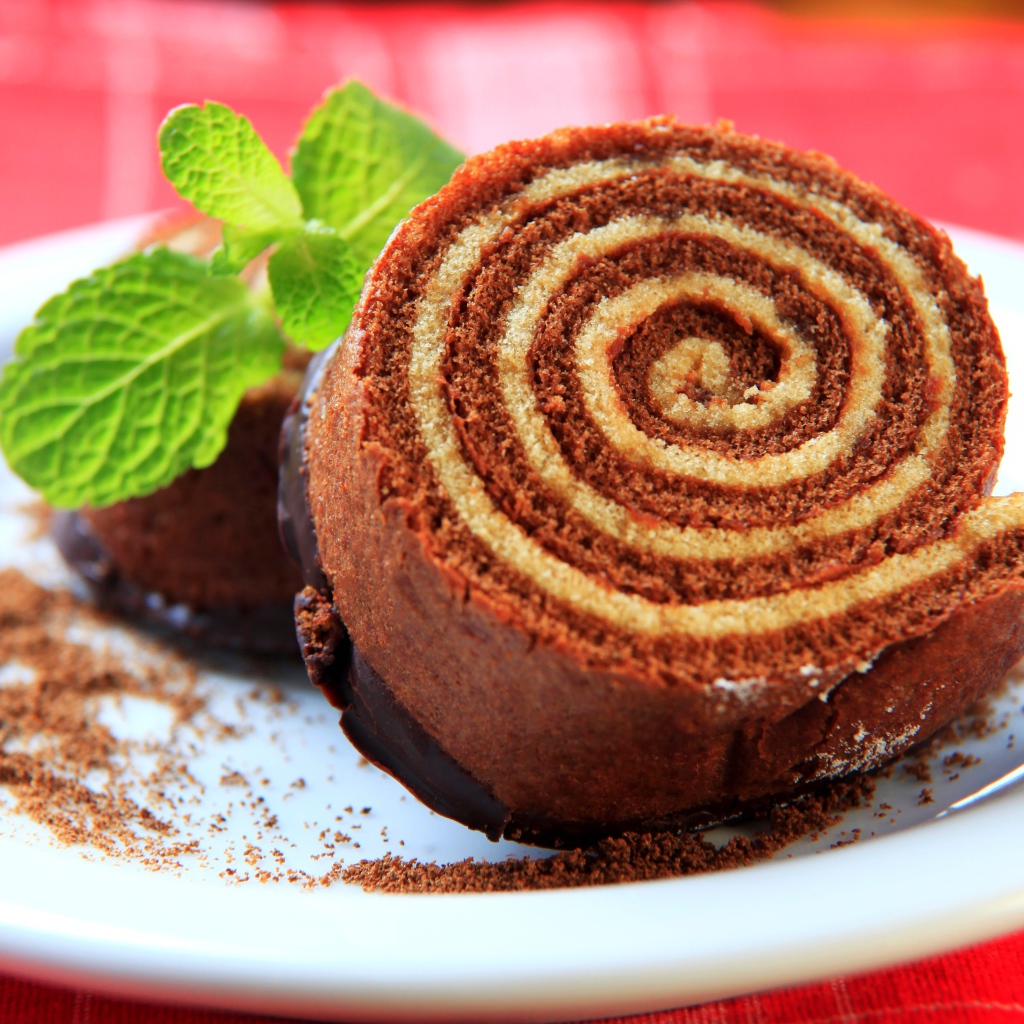 Кусок сладкого рулета с шоколадом и листом мяты на тарелке