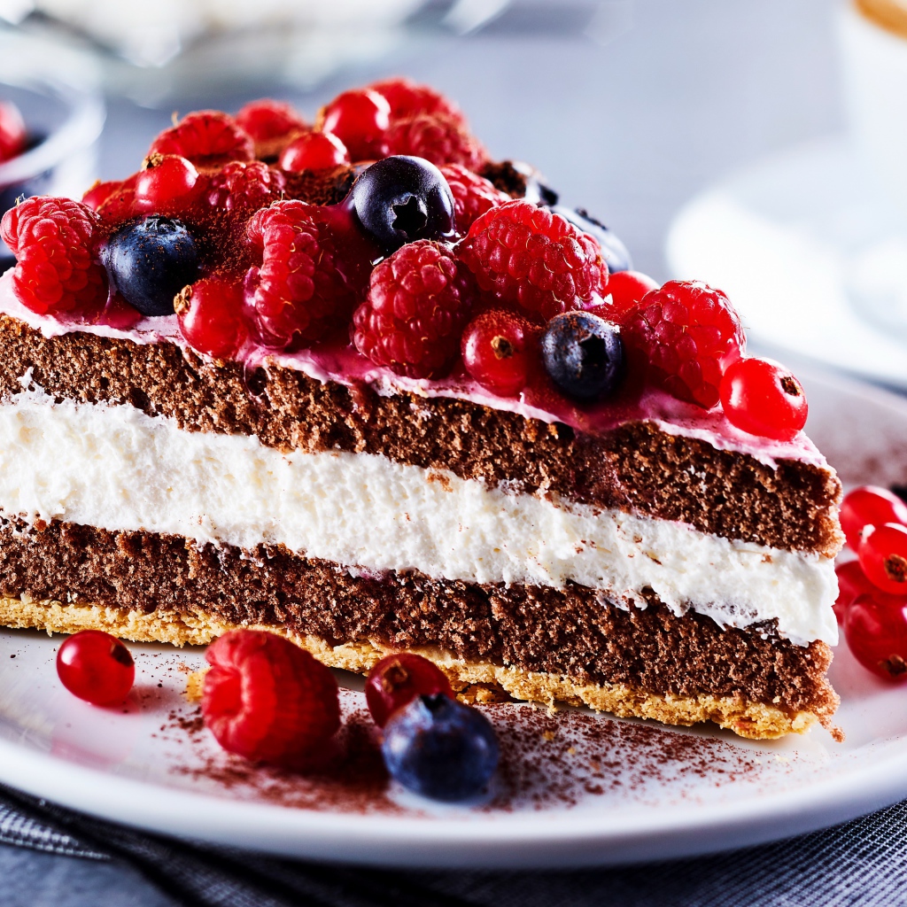 Аппетитный кусок торта на тарелке с ягодами малины, красной смородины и черники