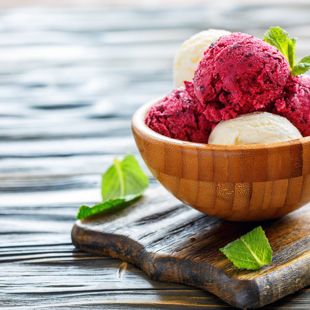 Шарики фруктового и ванильного мороженого в деревянной миске на столе