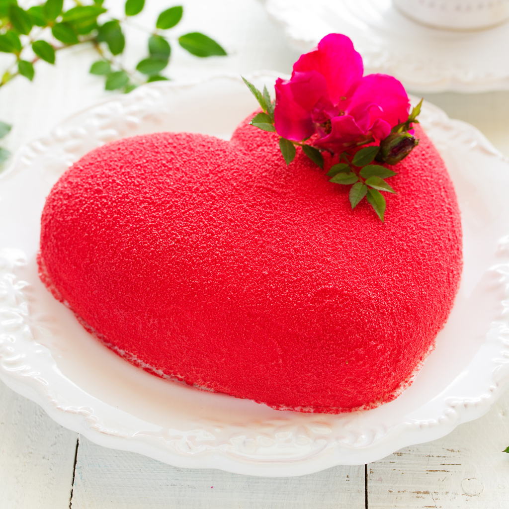 Красивый торт в форме сердца на белом блюде с красным цветком