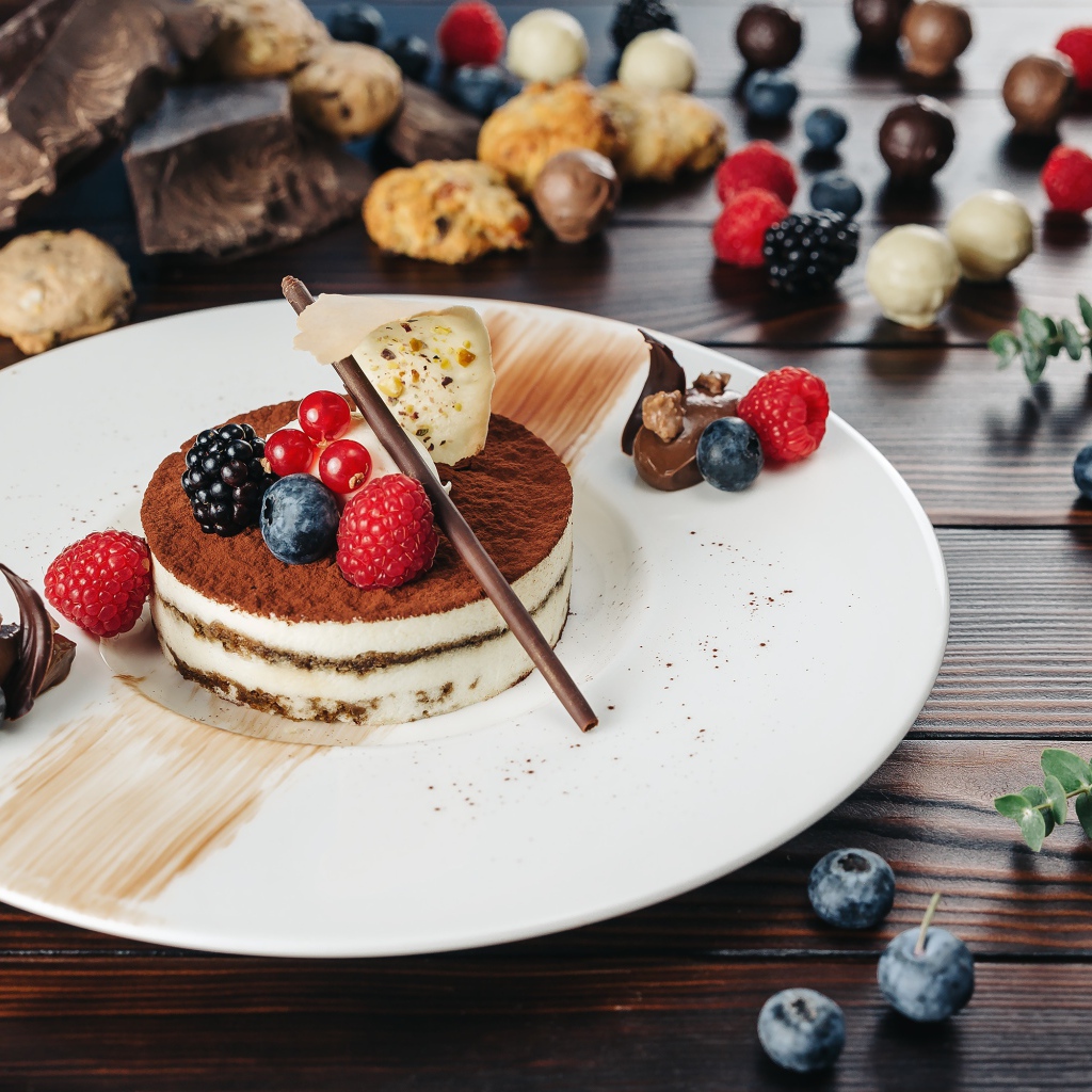 Пирожное с ягодами и шоколадом на белой тарелке 