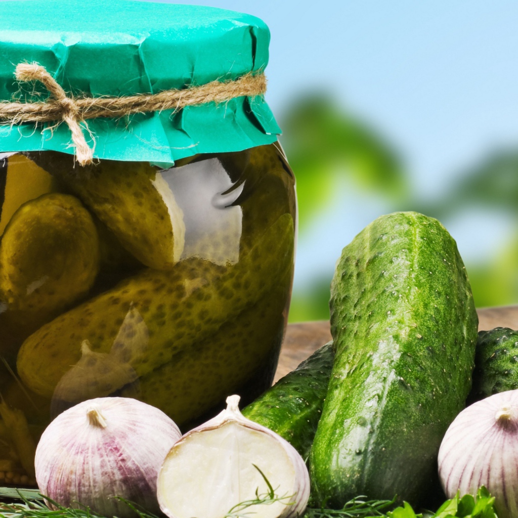 Консервированные огурцы в банке на столе со свежими огурцами и чесноком