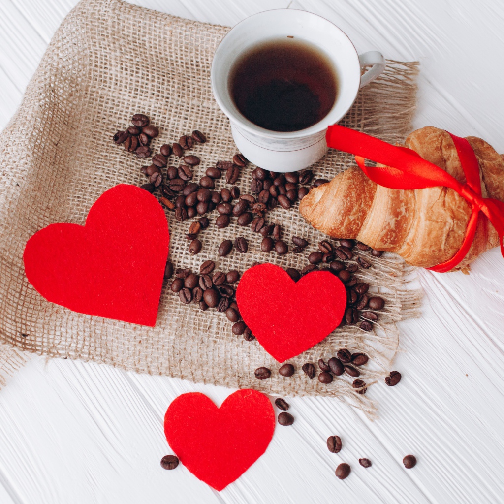 Круассан с чашкой кофе и кофейными зернами на столе с красными сердечками