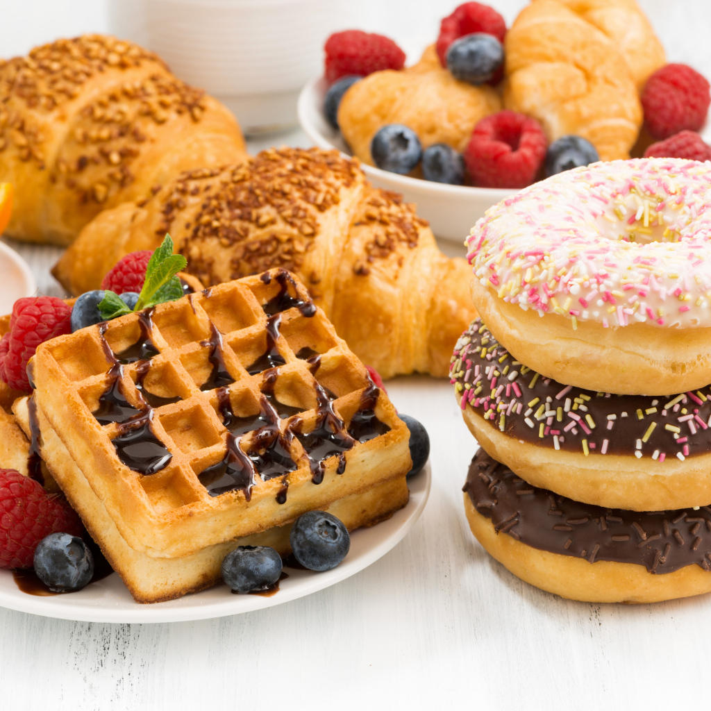 Круассаны, вафли и пончики на столе с ягодами
