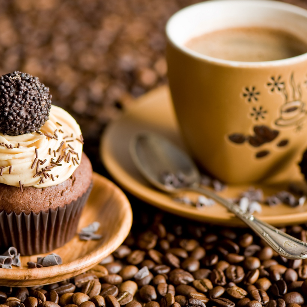 Кекс с кремом и чашкой кофе стоят на кофейных зернах 