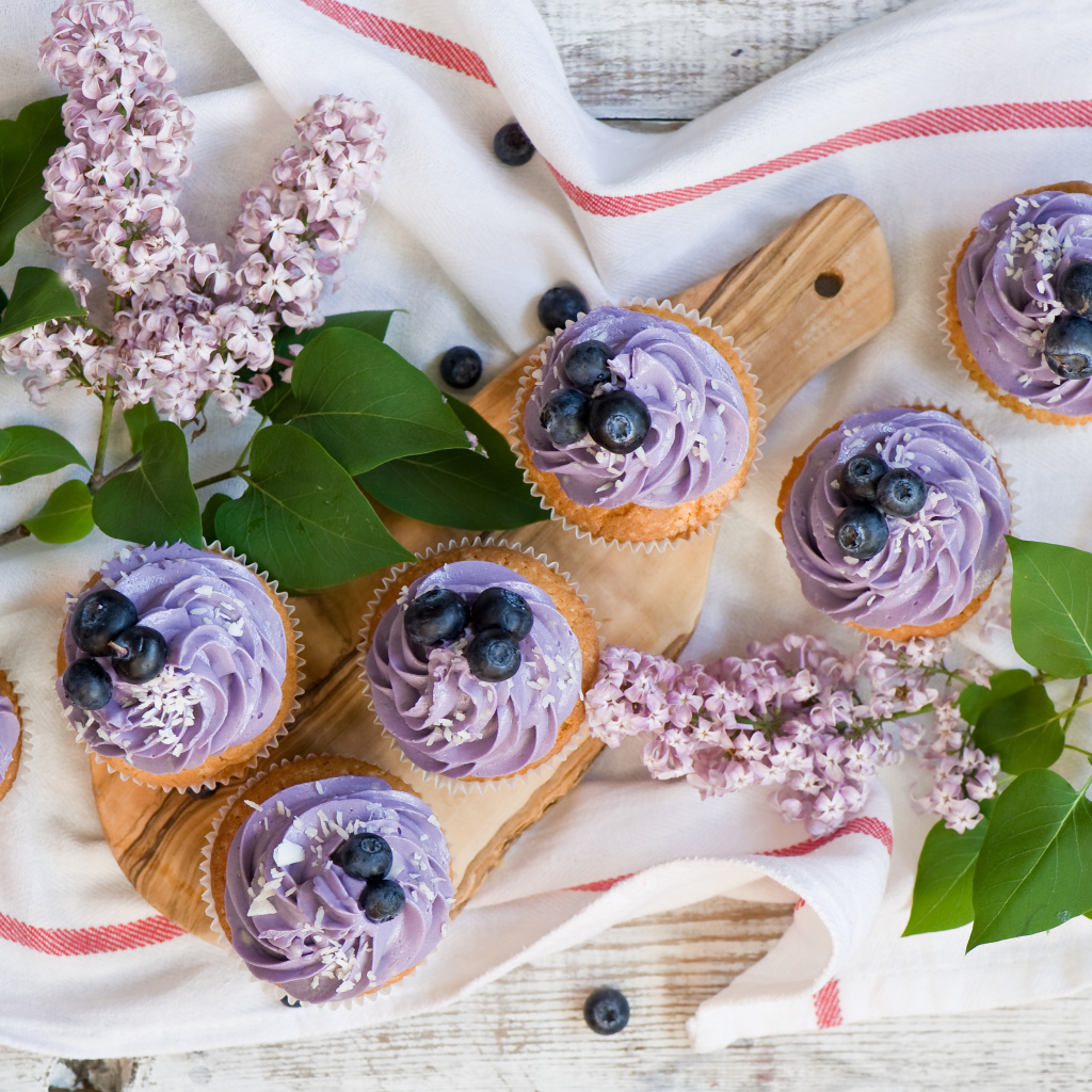 Кексы с кремом и ягодами черники на столе с ветками сирени 