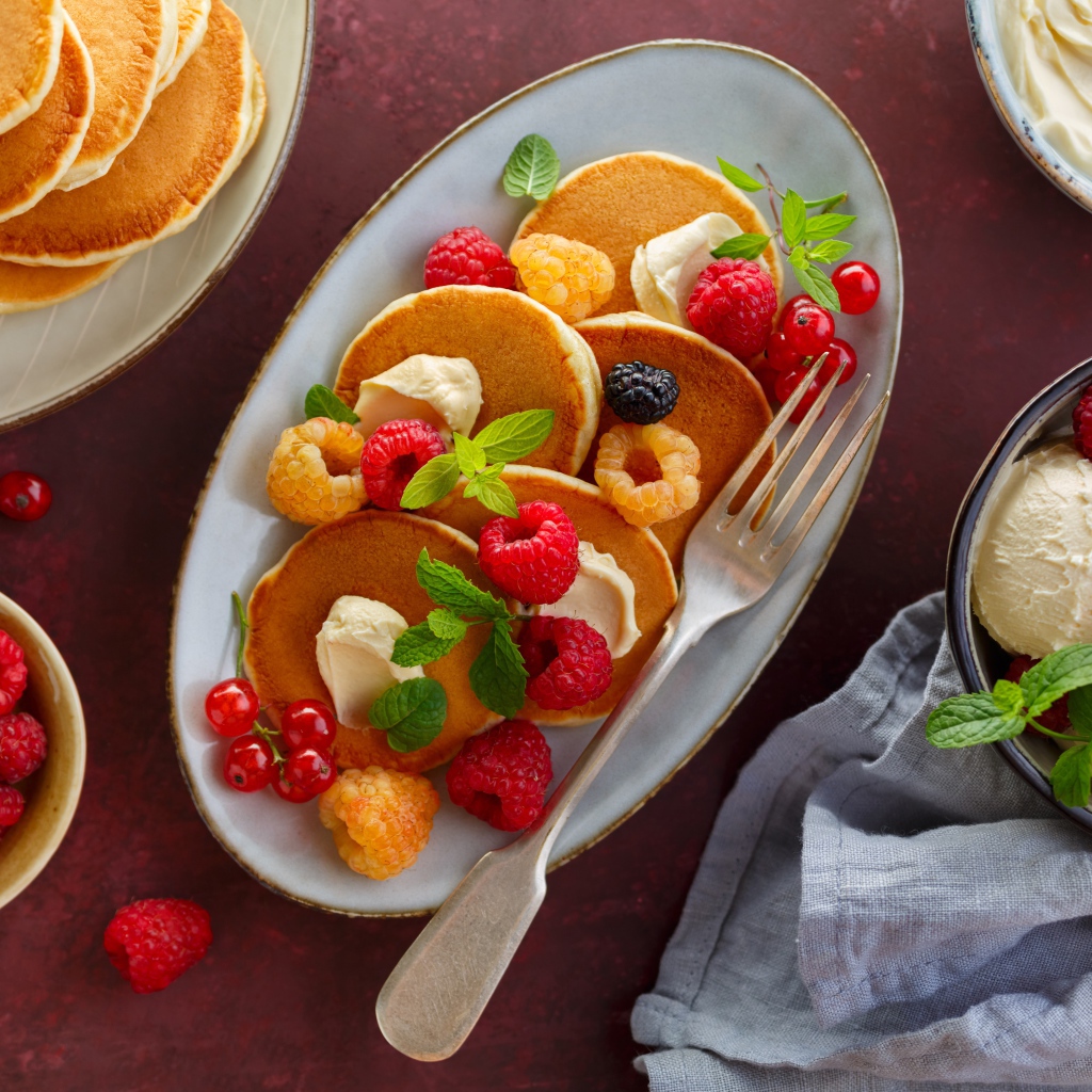 Оладьи на столе с ягодами малины и мороженым