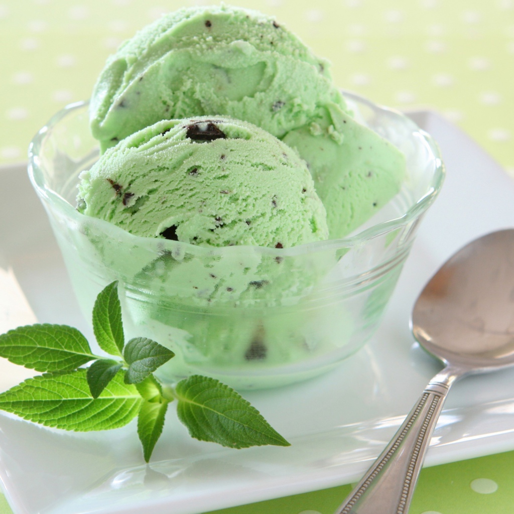 Зеленые шарики мороженого с шоколадом и мятой на тарелке с ложкой