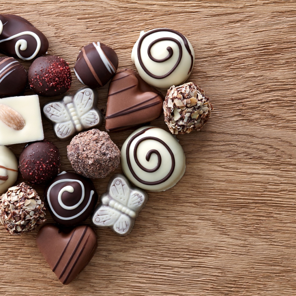 Сердце из шоколадных конфет ассорти на деревянном столе