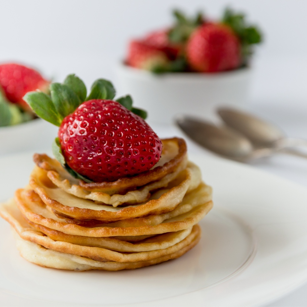 Оладьи с ягодами свежей клубники на белой тарелке 