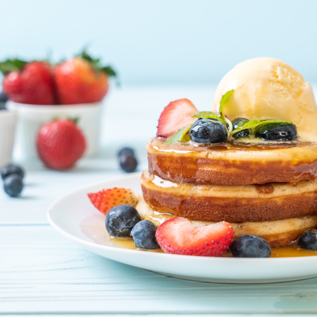 Оладья и медом, мороженым и ягодами черники и клубники на столе