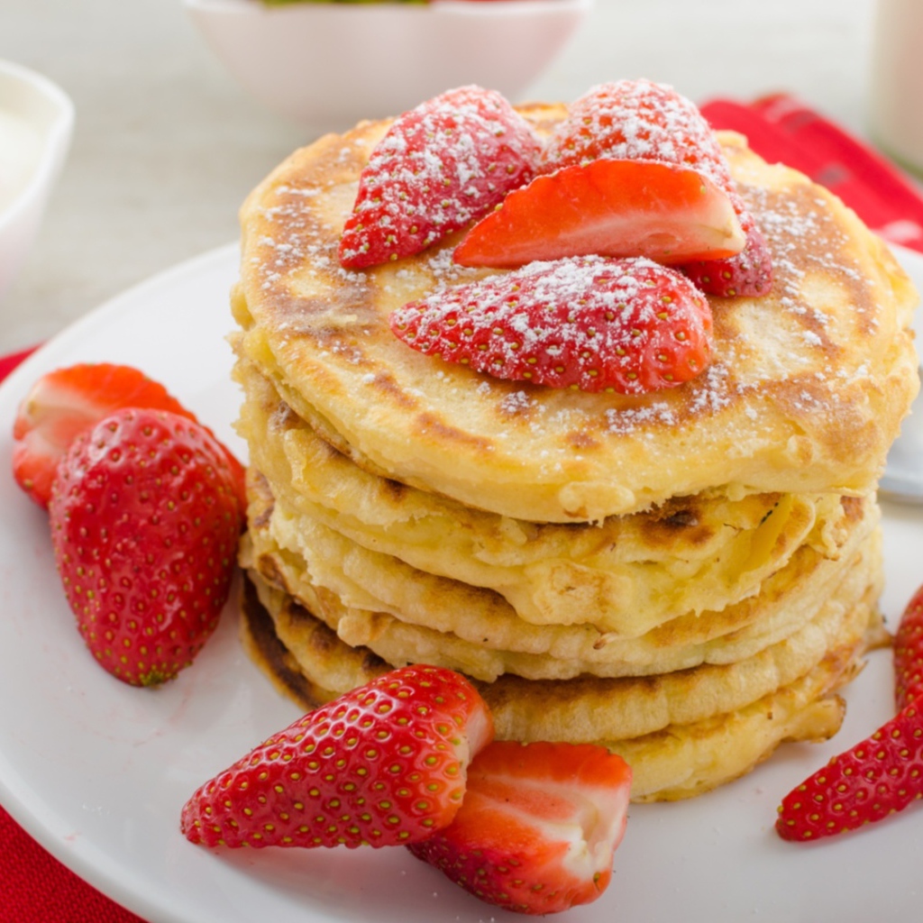 Оладьи с клубникой и сахарной пудрой на белой тарелке 