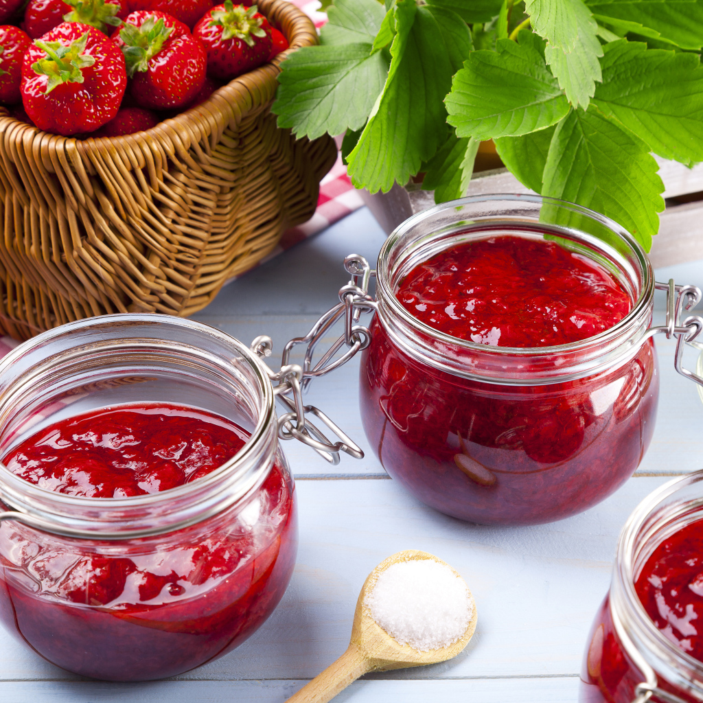 Клубничное варенье в стеклянных баночках на столе  ягодами