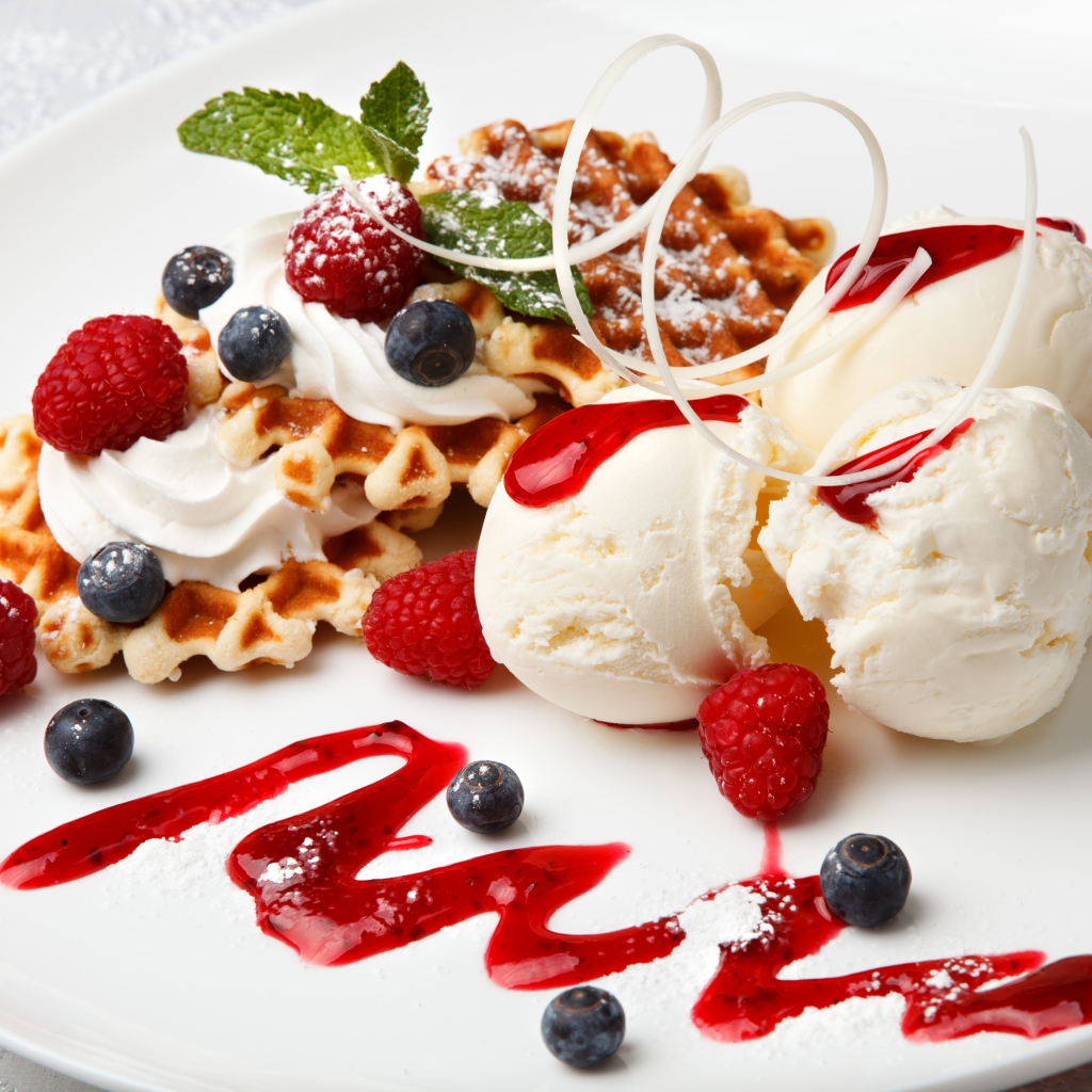Сладкие вафли с ягодами черники и малины на белой тарелки с шариками мороженого