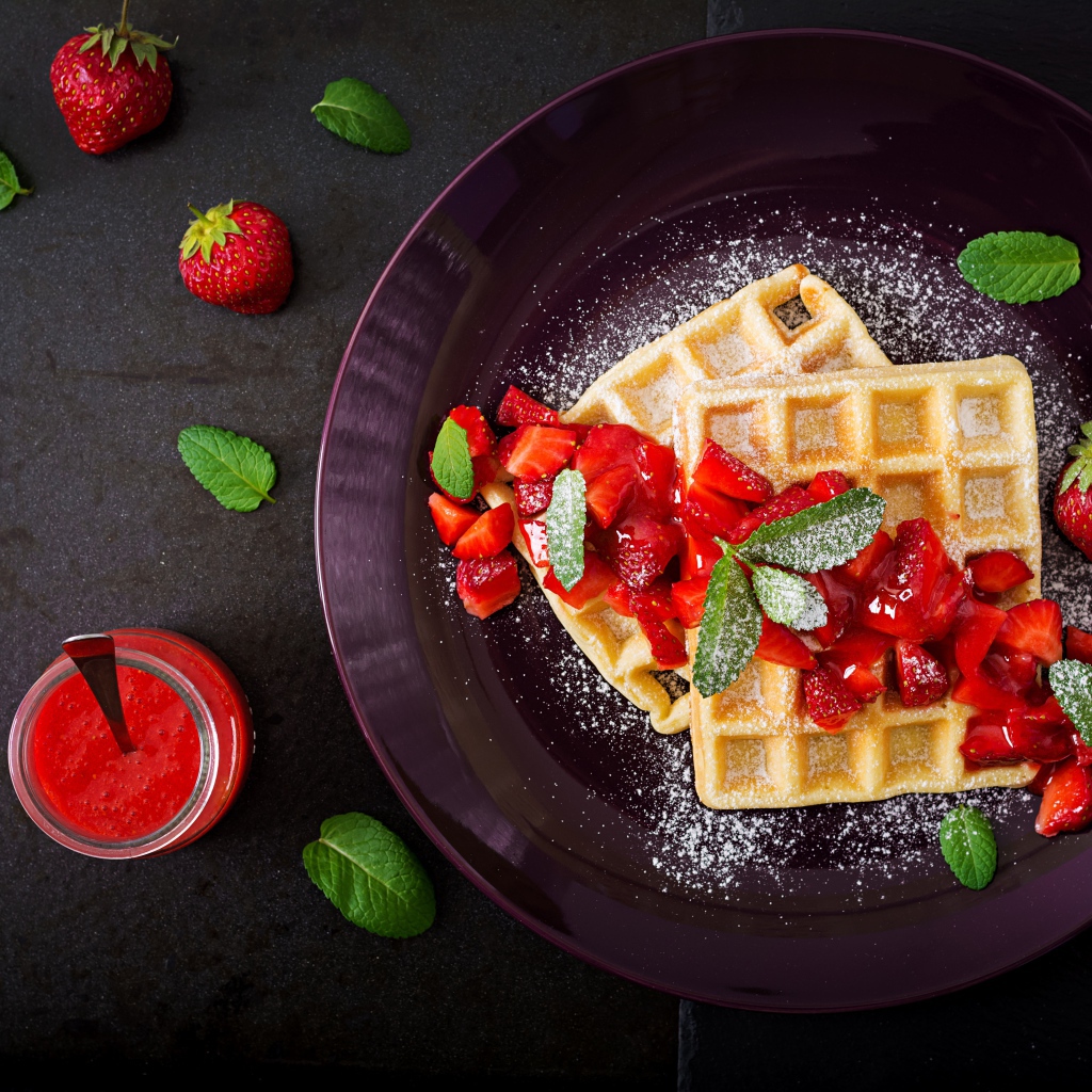 Сладкие вафли с клубникой и сахарной пудрой на тарелке 