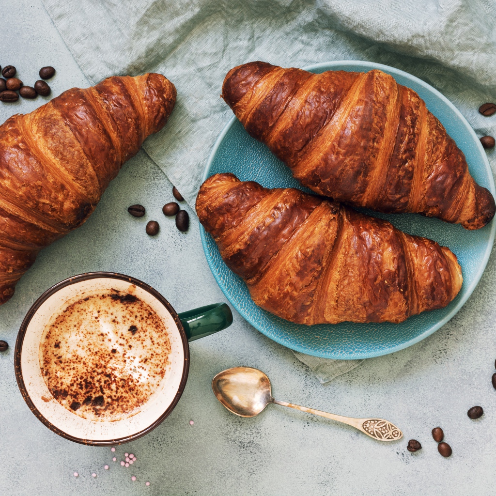 Три круассана на столе с чашкой кофе